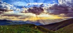 Sonne strahlt durch die Wolken über bergiger Landschaft